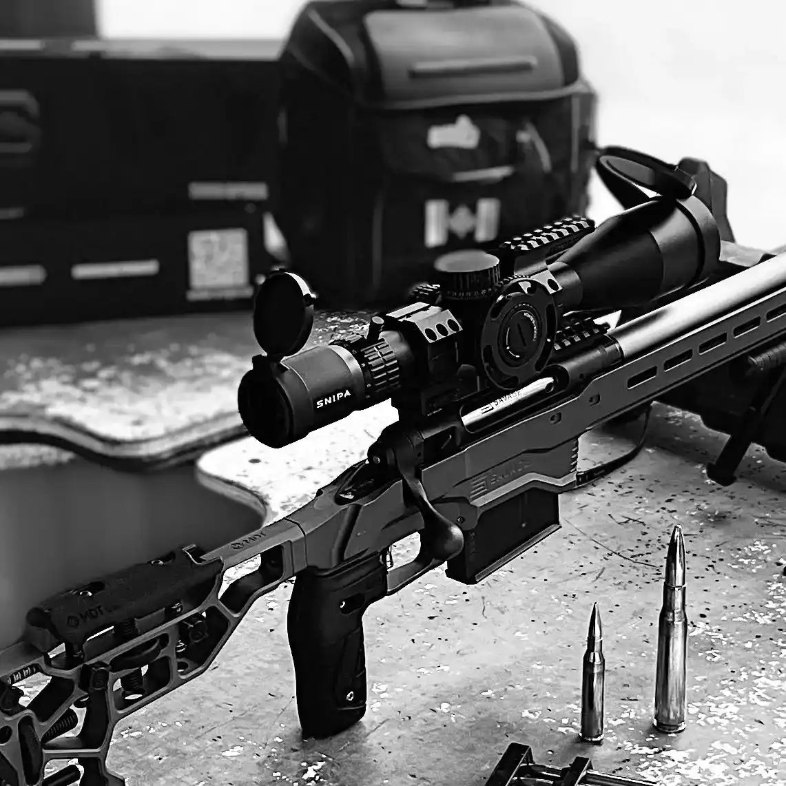 SNIPA Northline tactical precision rifle scope mount with integrated level and top Picatinny rail on a modern rifle, shown on a shooting bench beside two large rifle cartridges. TUTT