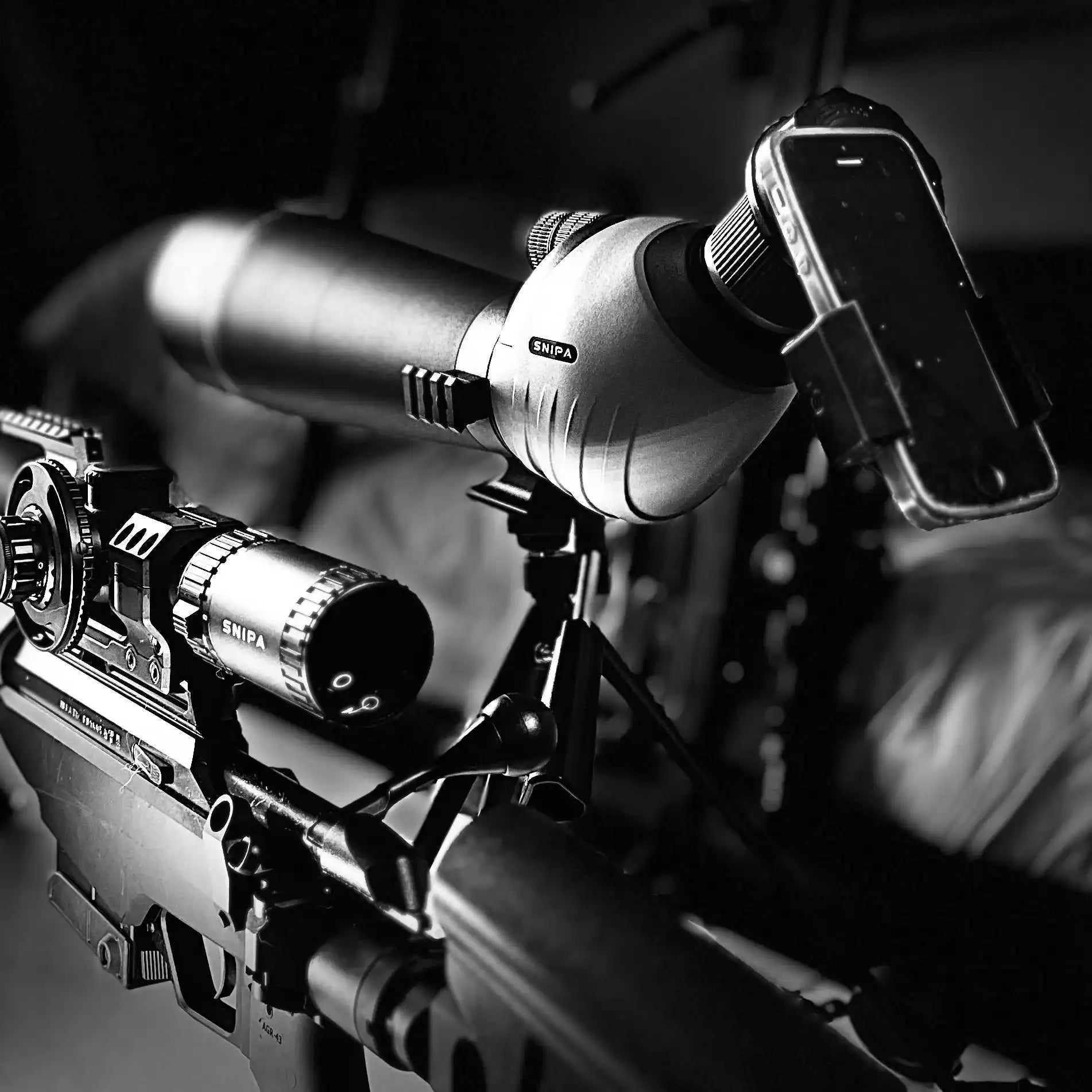 SNIPA spotting scope with phone adapter on tripod beside rifle indoors, tactical setup TUTT
