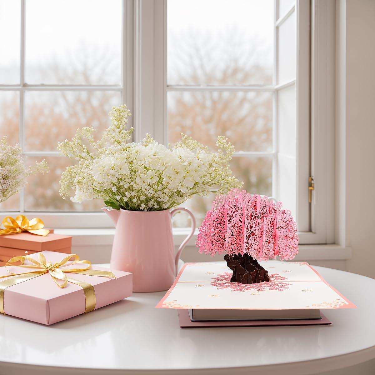 Pop-up pink cherry blossom greeting card with gifts and white flowers on a table, TUTT