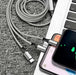 3-in-1 charging cable plugged into smartphone and laptop on grey carpet, travel tech kit TUTT