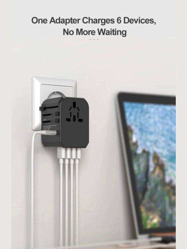 Universal travel adapter plugged into wall outlet charging multiple devices, laptop on desk, TUTT